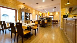 A restaurant with wooden flooring, multiple dining tables, and chairs. There are shelves with bottles and a counter with a mirror. - Aparthotel Capitolina (Merida)