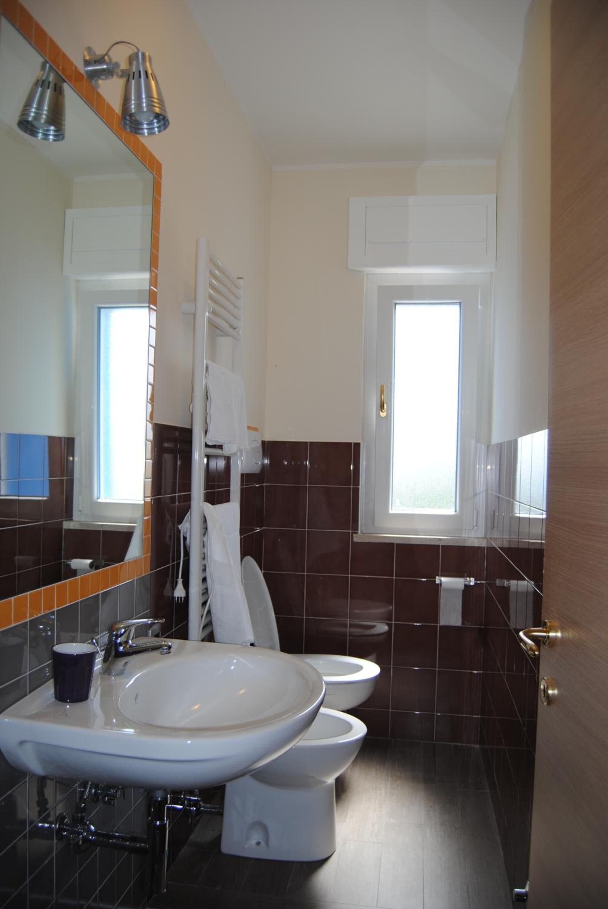 A bathroom with a large sink, two toilets, a mirror, and a window.