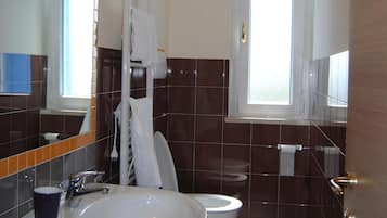 A bathroom with a large sink, two toilets, a mirror, and a window.