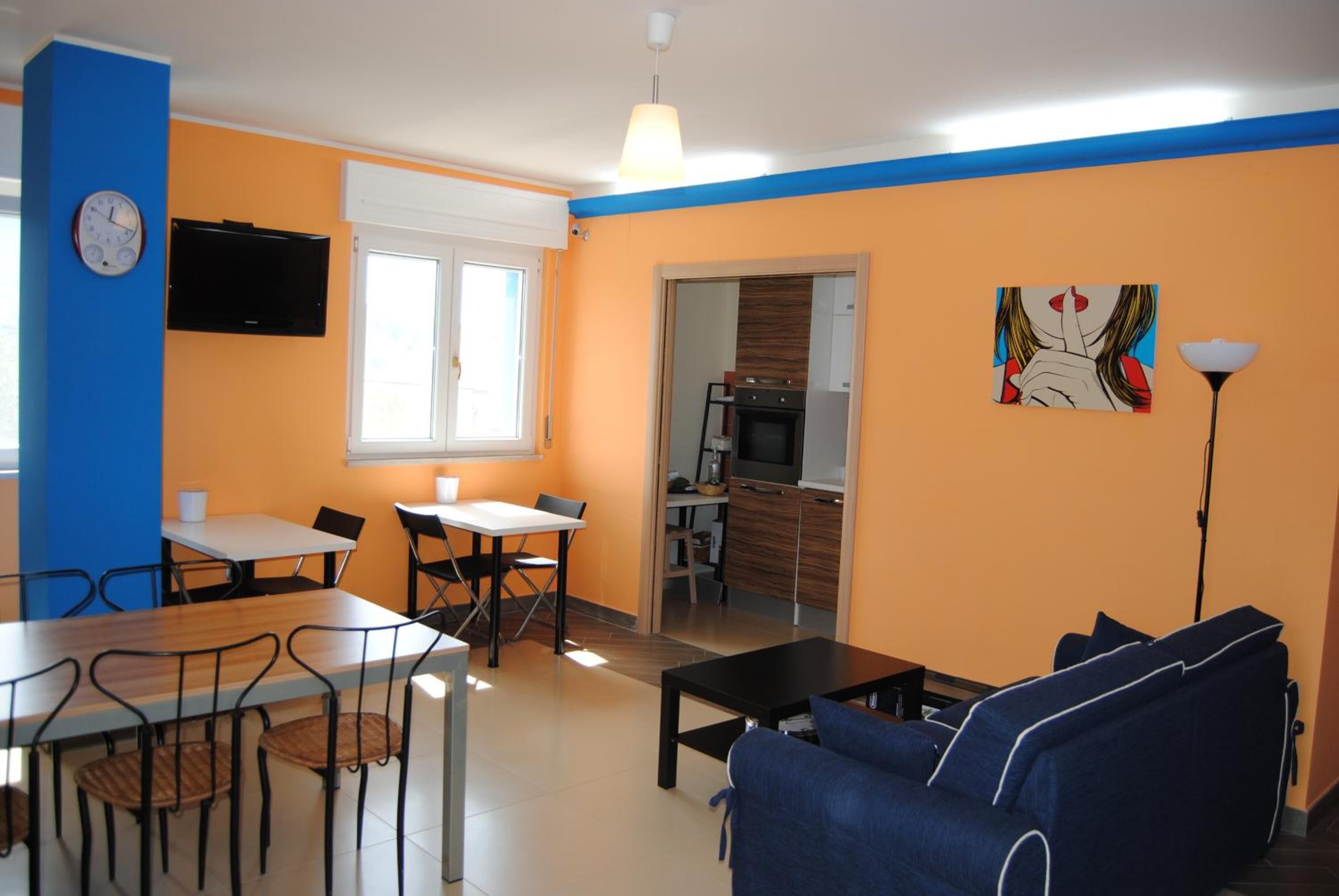 Un salon avec un canapé bleu, un coin repas avec une table et des chaises, un coin cuisine avec une cuisinière et un four, et un téléviseur fixé au mur.
