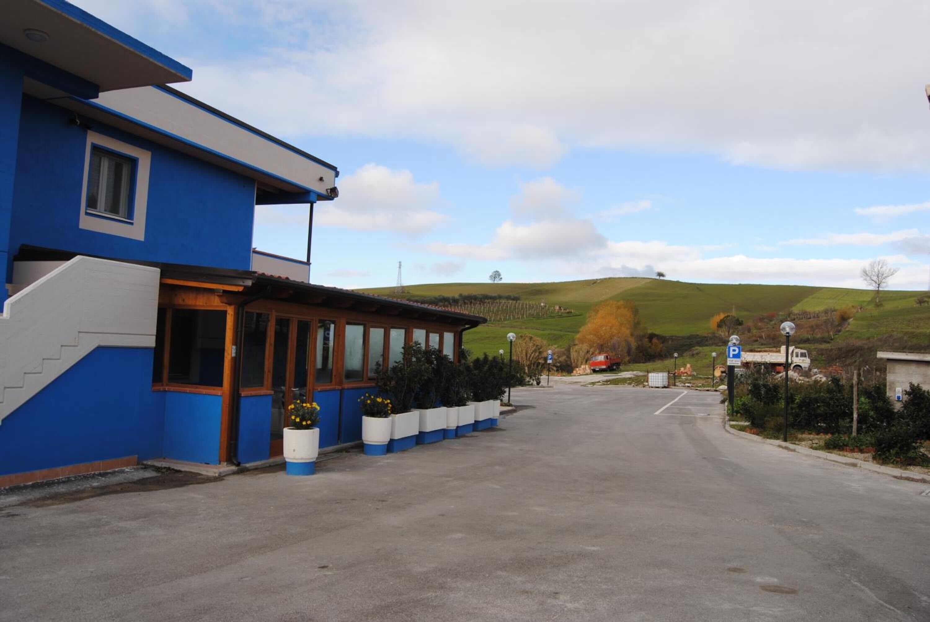 A blue building with a parking area and a view of green hills in the background.