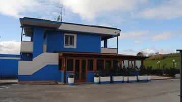 Un edificio a due piani con facciata blu e bianca, una piccola finestra e un'area d'ingresso coperta con piante in vaso.