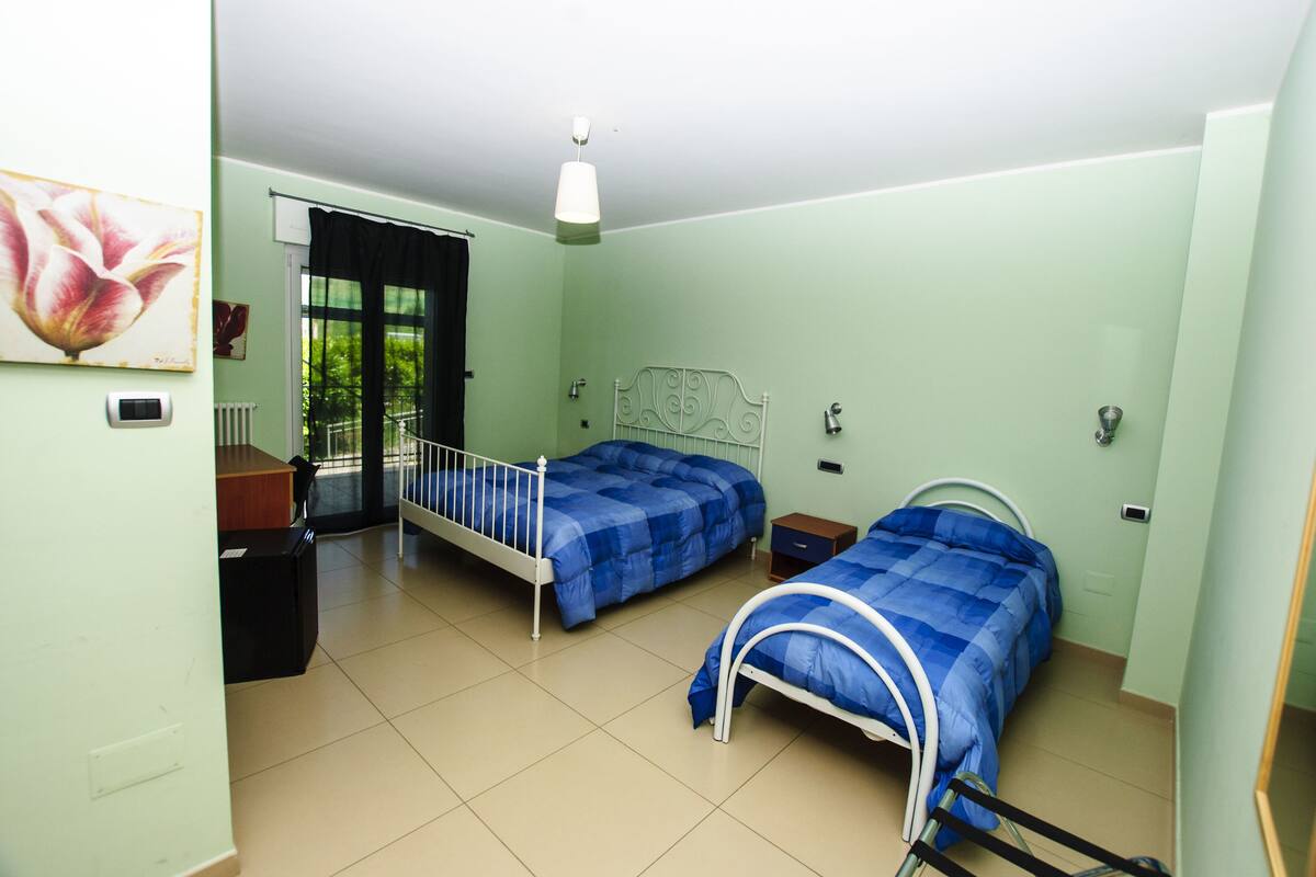 Un dormitorio con dos camas, un escritorio, una silla, un radiador y una ventana con cortinas.