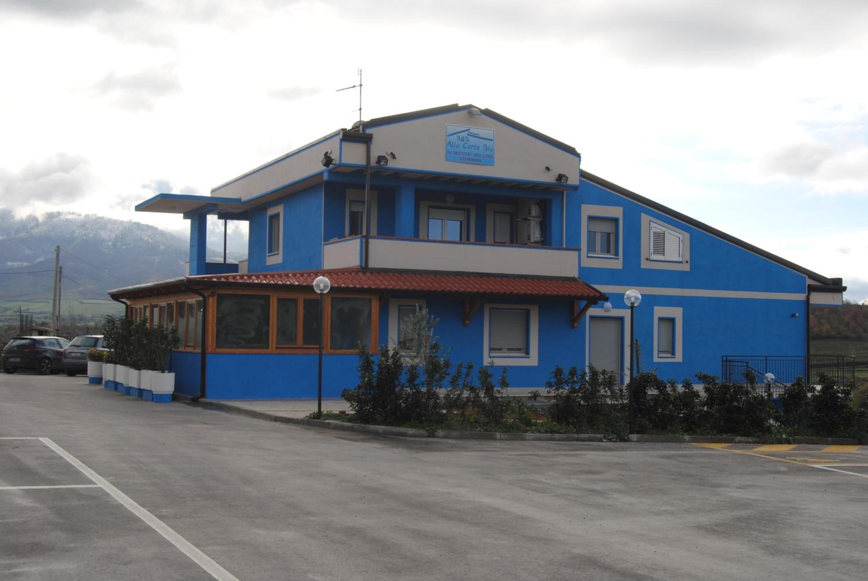 Un edificio de dos plantas con fachada azul, techo de tejas rojas y un letrero que indica que es un hotel.