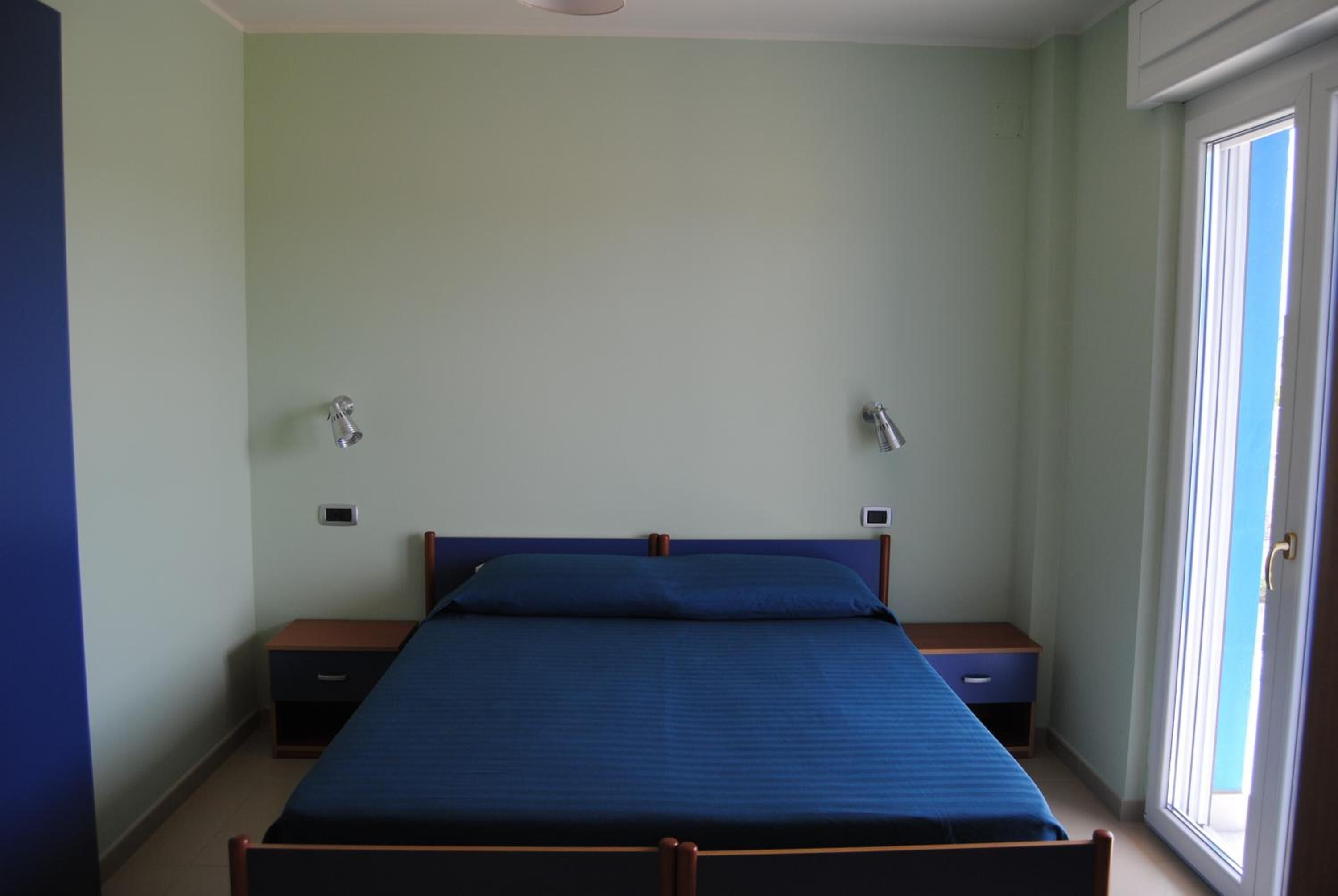 A bedroom with a single bed, two bedside tables, and a window.