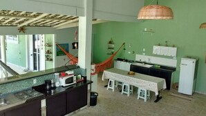 A kitchen with a gas stove, a microwave, and a sink. There is a dining table with four stools. A hammock is hanging in the room. - Hostel Clube da Aventura (Conde)