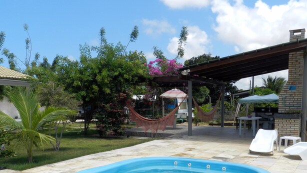A swimming pool with a pergola and hammock, surrounded by greenery and a brick building. - Hostel Clube da Aventura (Conde)