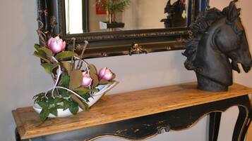 Una consola de madera con un espejo negro decorativo encima, una escultura de un caballo ornamental y un jarrón con flores rosadas.