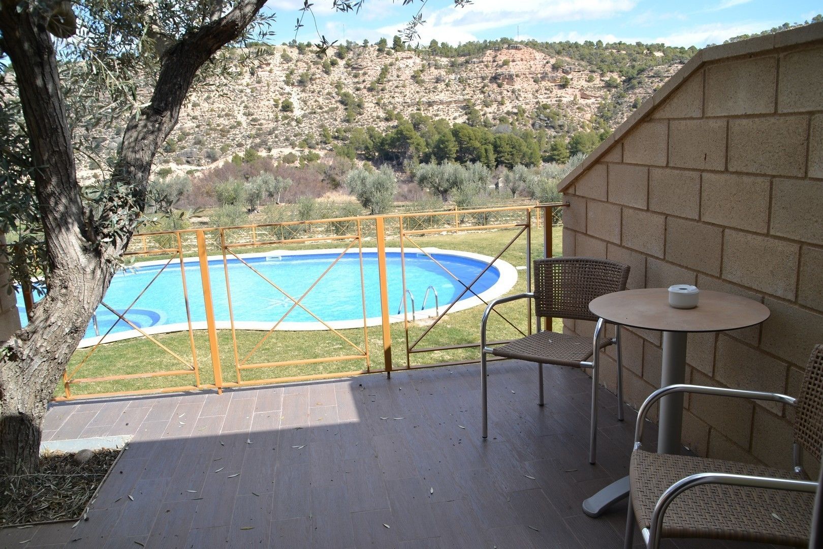 Un balcone con vista su una piscina, due sedie in vimini e un tavolino.