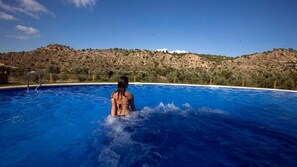 Une piscine à l’eau d’un bleu limpide, entourée d’une clôture, avec un paysage vallonné en arrière-plan.