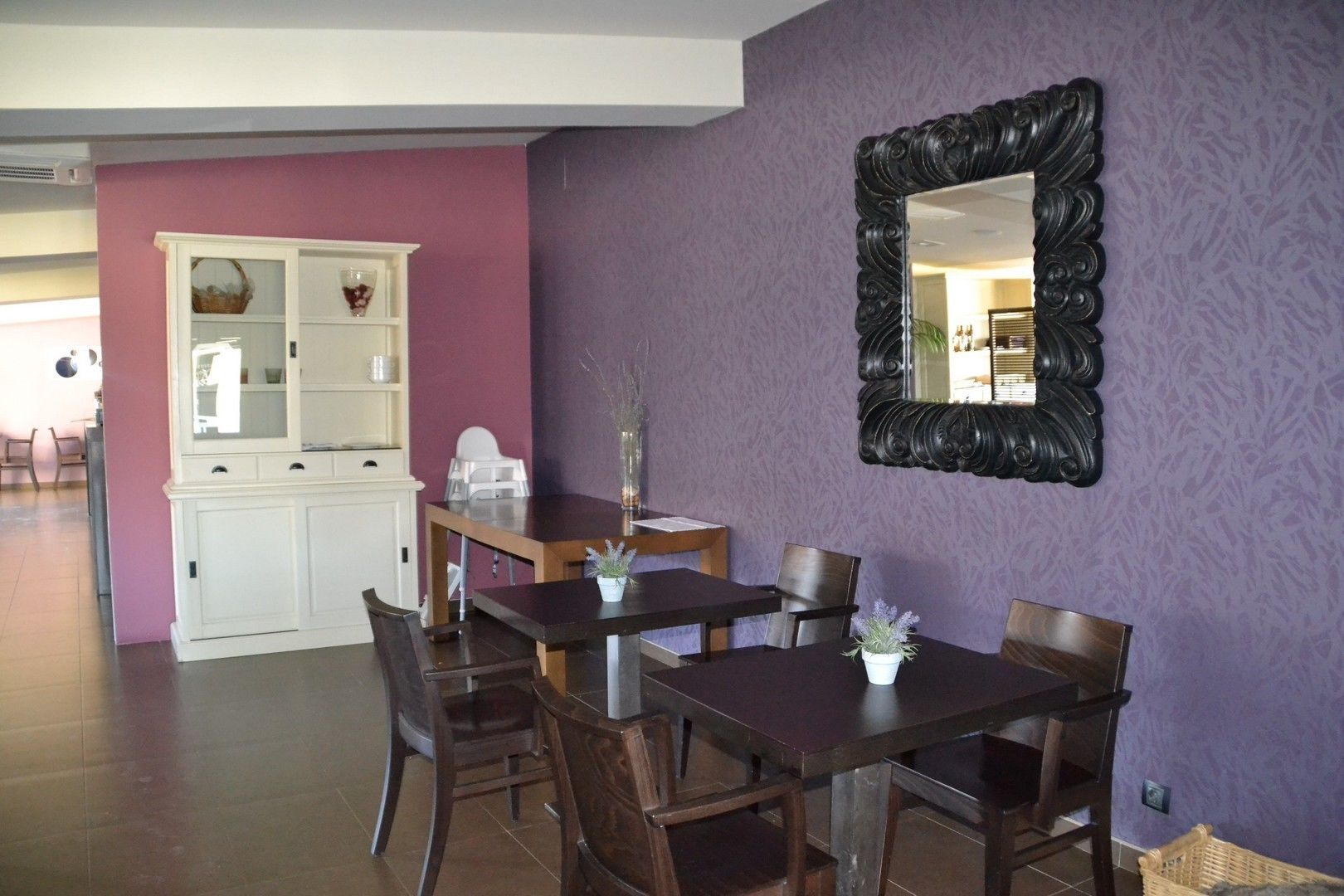 Un coin repas avec une table et des chaises, un buffet blanc aux portes vitrées et un miroir au mur.