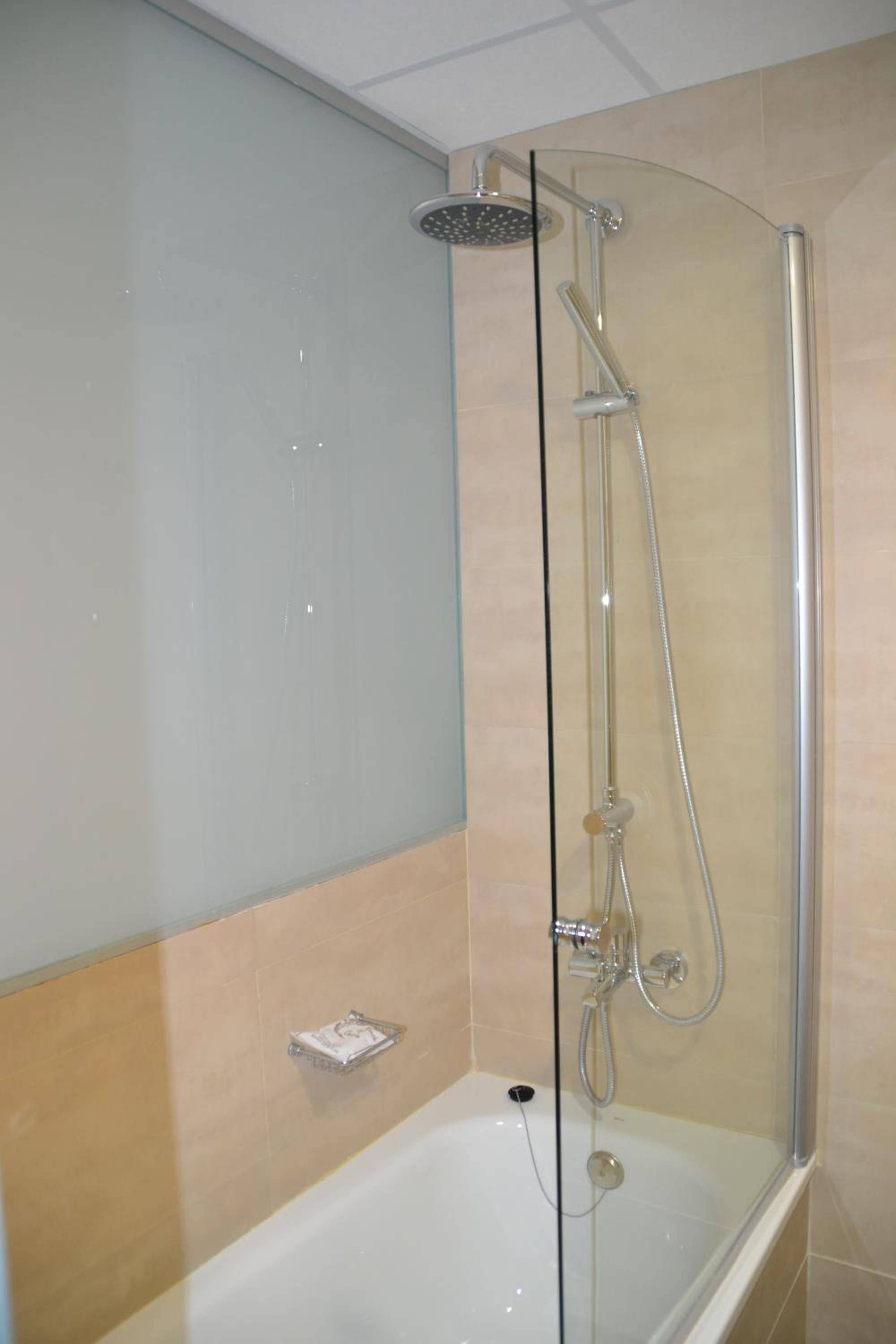 A glass-enclosed shower with a handheld showerhead and a handheld faucet.