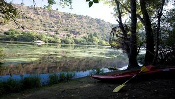 A calm river with a red canoe and paddle, surrounded by trees and a hilly landscape.