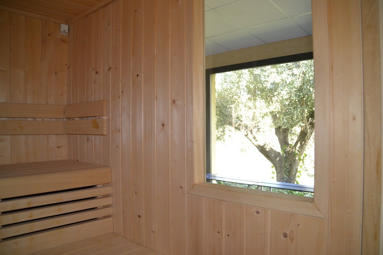 Une pièce en bois avec une grande fenêtre, un banc intégré et une bouche d’aération au plafond.