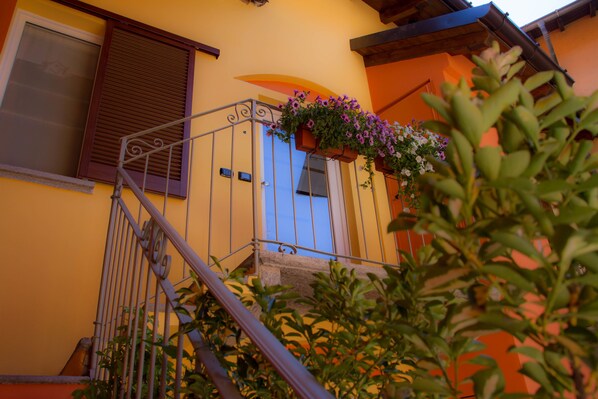 Un edificio amarillo con puerta azul, escaleras de metal y una jardinera en el balcón.