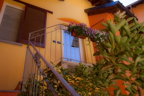 A yellow building with a blue door, a metal staircase, and a flower box on the balcony.