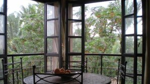 A round table with a metal frame and red cushions, positioned in a corner with large windows offering a view of greenery outside. - Appart avec vue Jardin-Majorelle (Marrakech)