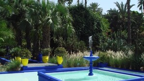 A blue-tiled pool with a central fountain surrounded by yellow planters and lush greenery. - Appart avec vue Jardin-Majorelle (Marrakech)
