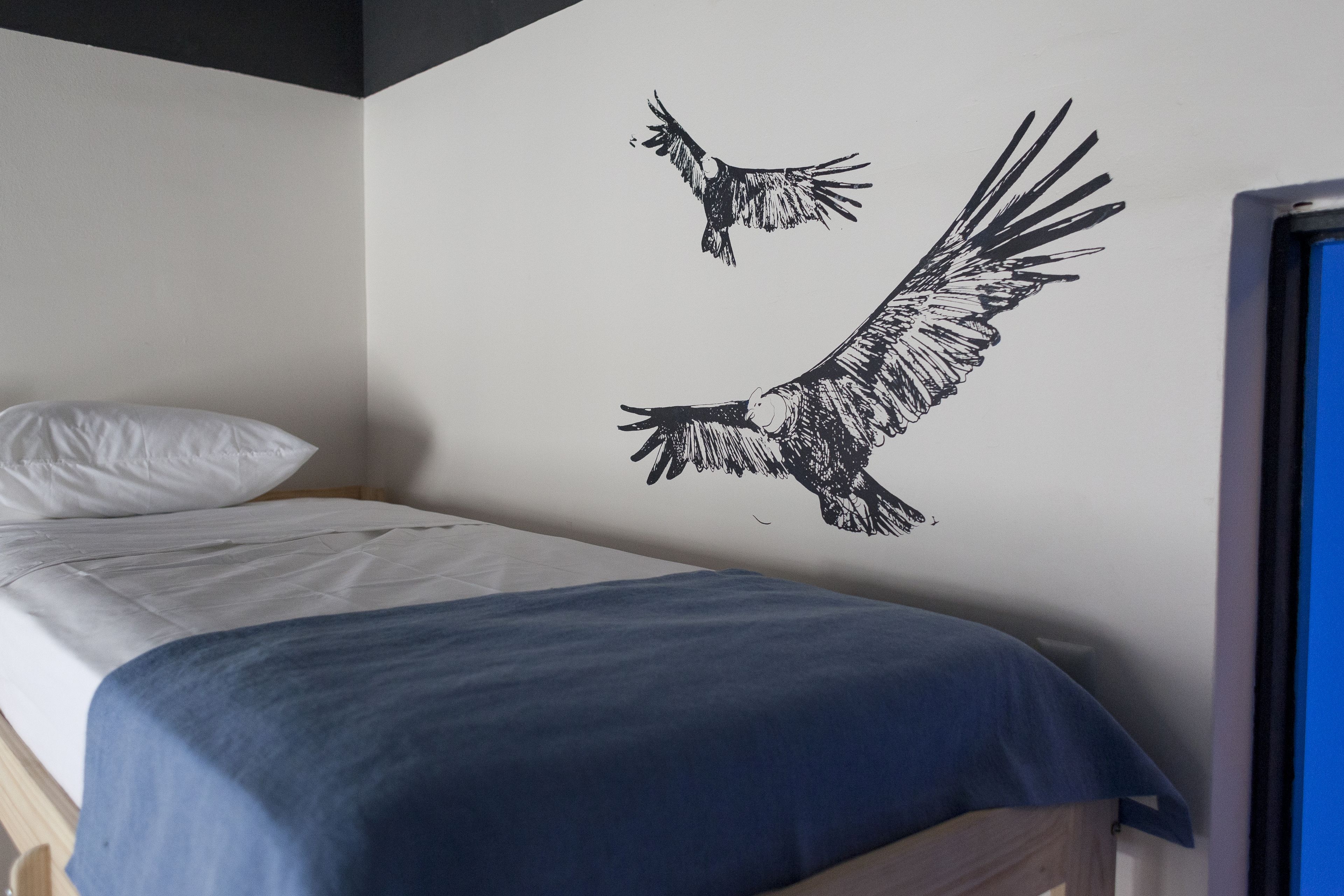 Une chambre à coucher avec un lit, une couvre-lit bleue et un motif décoratif représentant un oiseau en vol sur un mur.