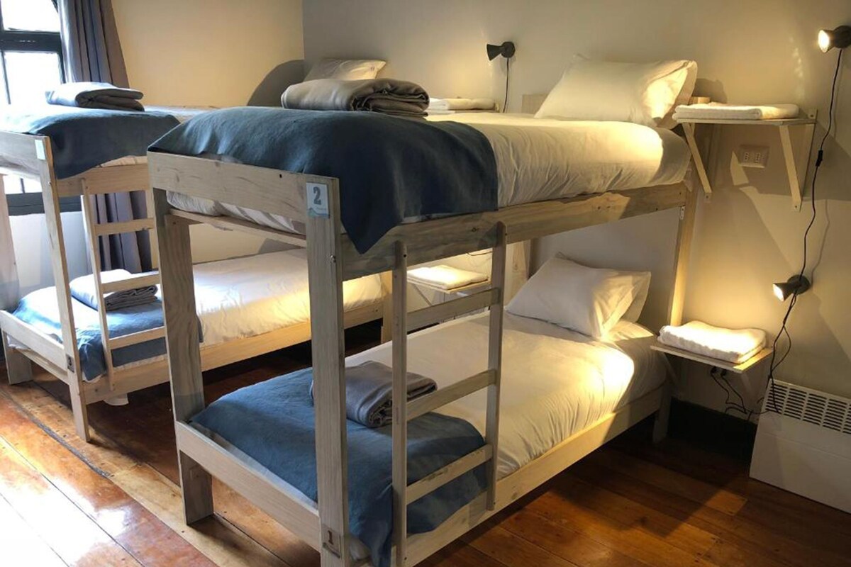 Una habitación con literas, una mesita de noche con lámpara y una ventana con cortinas.