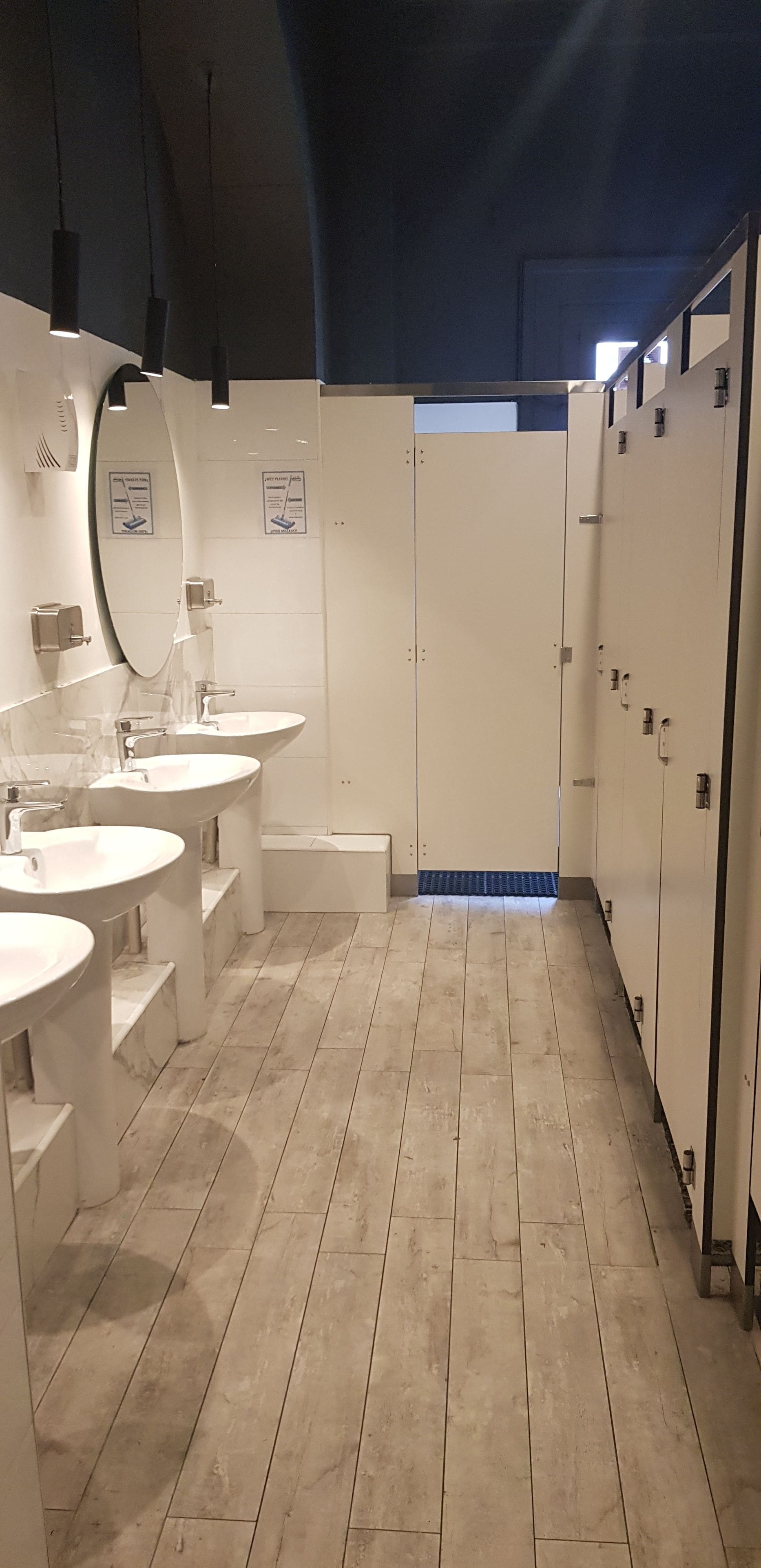 Un baño moderno con tres lavamanos, un espejo grande y una ducha a ras de suelo.