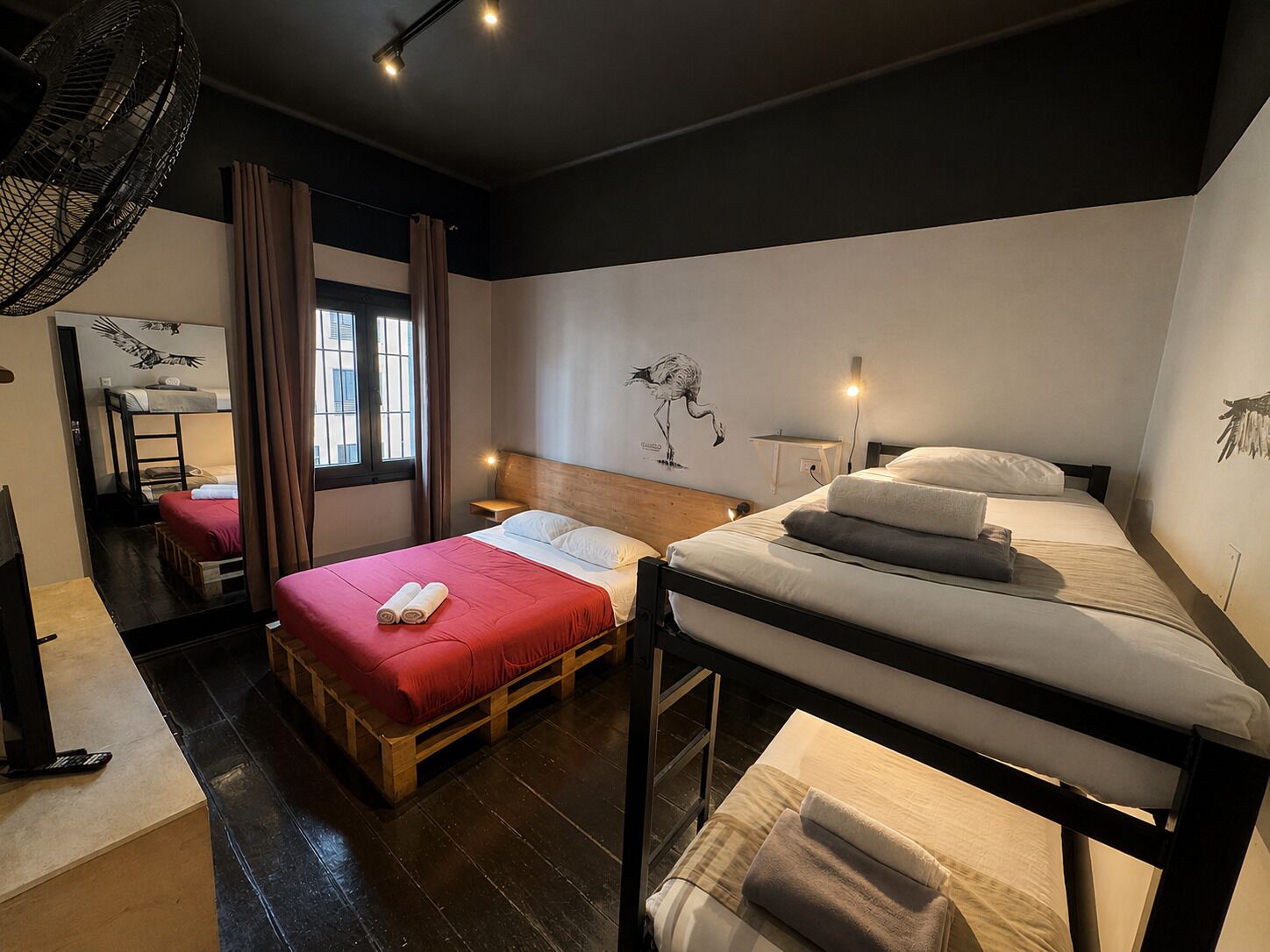 Quarto estilo dormitório com beliches, uma escrivaninha e uma janela com cortinas.
