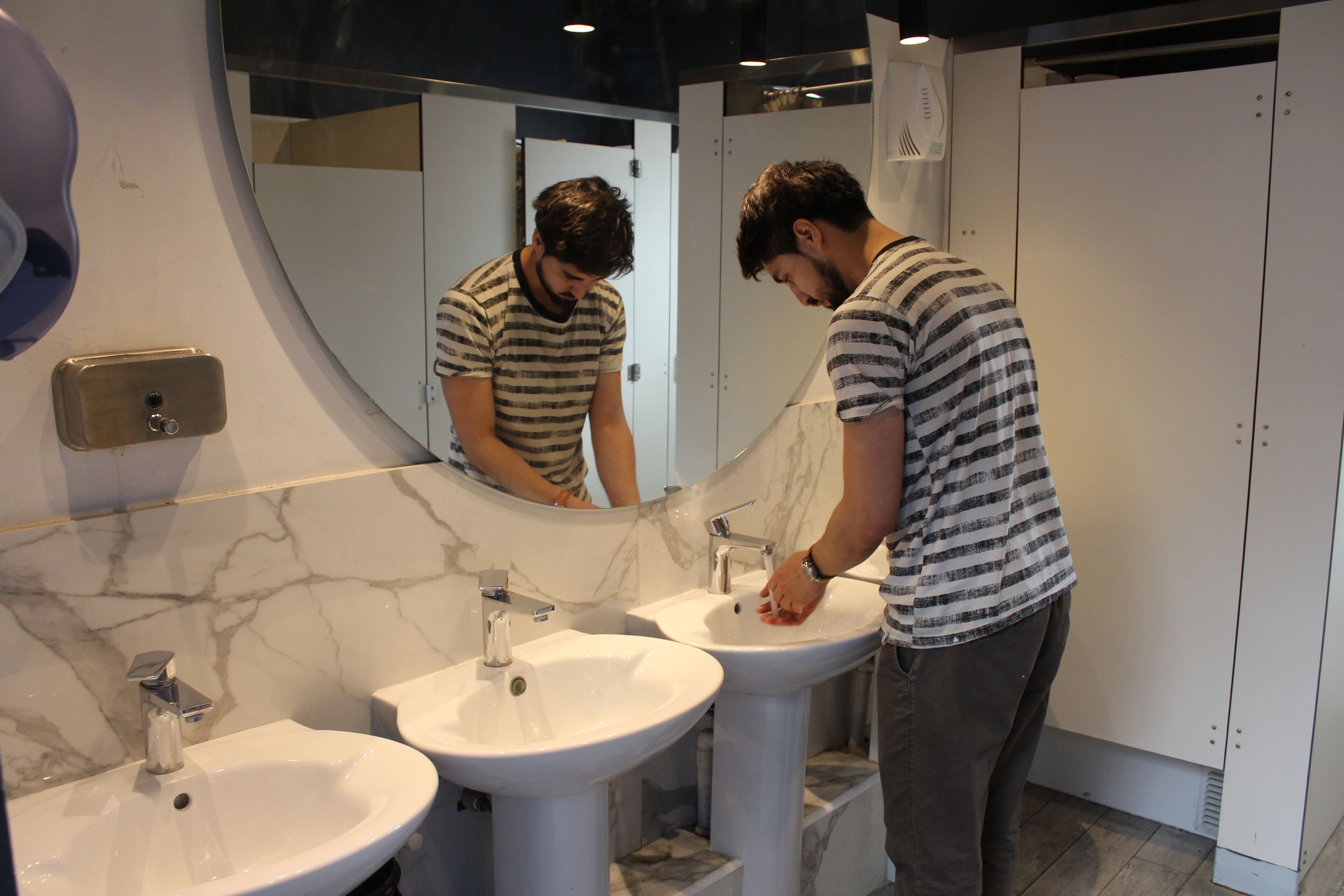 Un baño con dos lavamanos, un espejo y un secamanos.