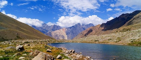 Paisaje montañoso con un lago, terreno rocoso y cielos despejados.