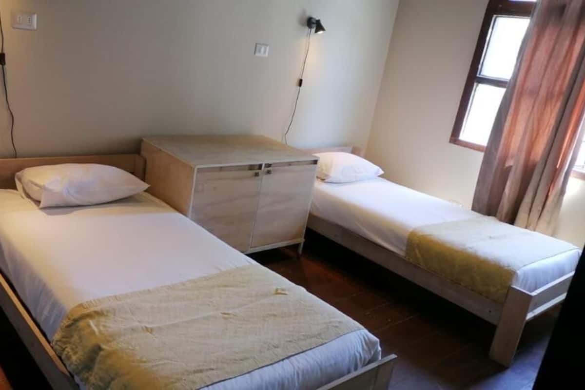A room with two single beds, a wooden cabinet, and a window with curtains.