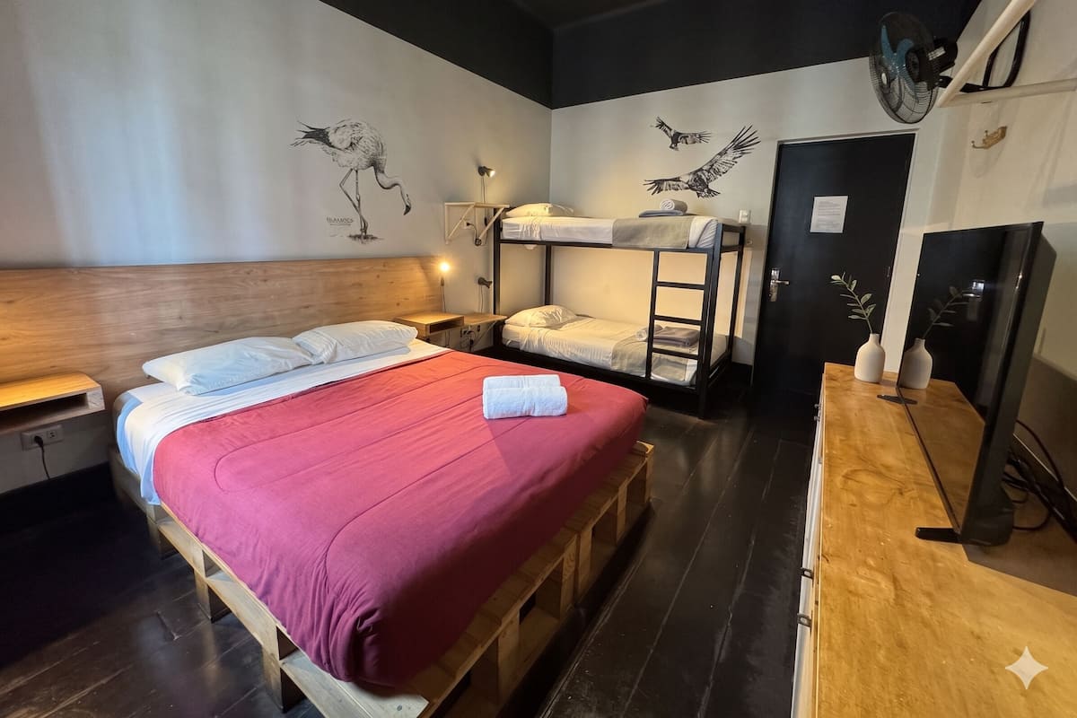 A room with a bunk bed, a single bed, a desk with a chair, a mirror, and wall art.