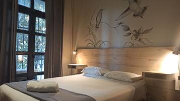 A bedroom with a wooden headboard, a bed with white linens, a bedside table with a lamp, and a window with curtains.