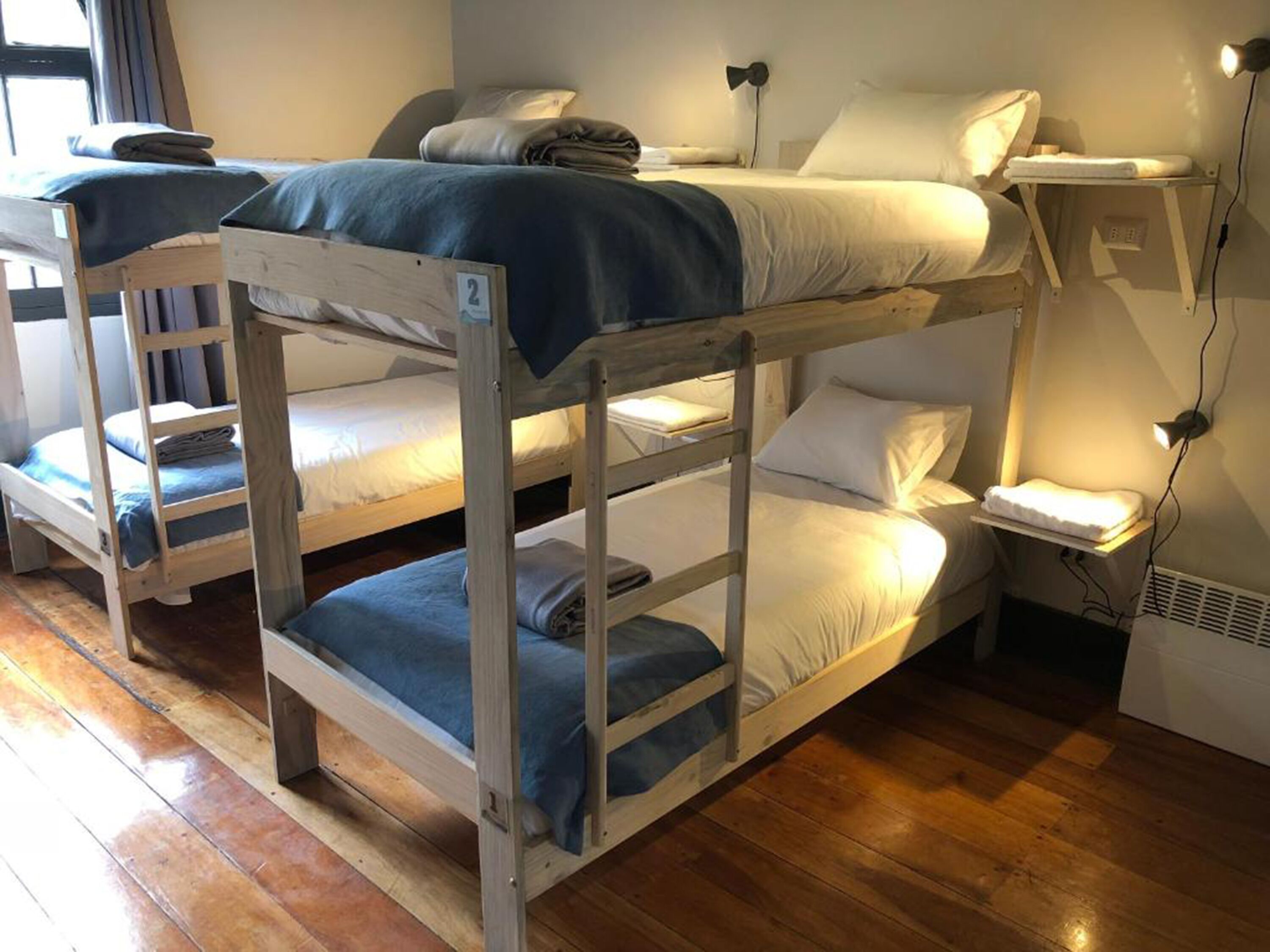 A room with bunk beds, a bedside table with a lamp, and a window with curtains.