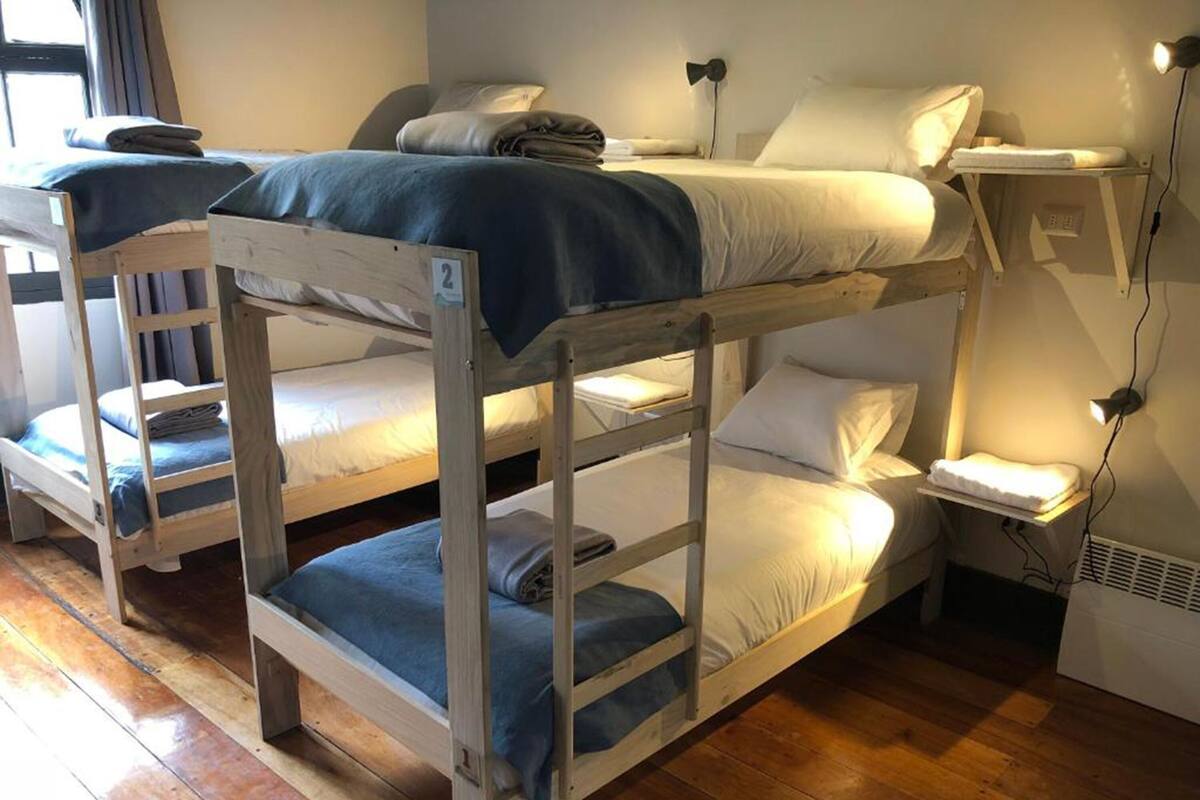 A room with bunk beds, a bedside table with a lamp, and a window with curtains.