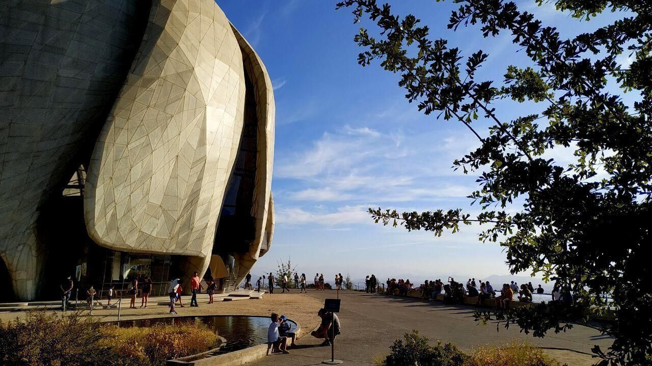 A modern architectural structure with a unique, curved design, surrounded by a public space with people and a body of water.