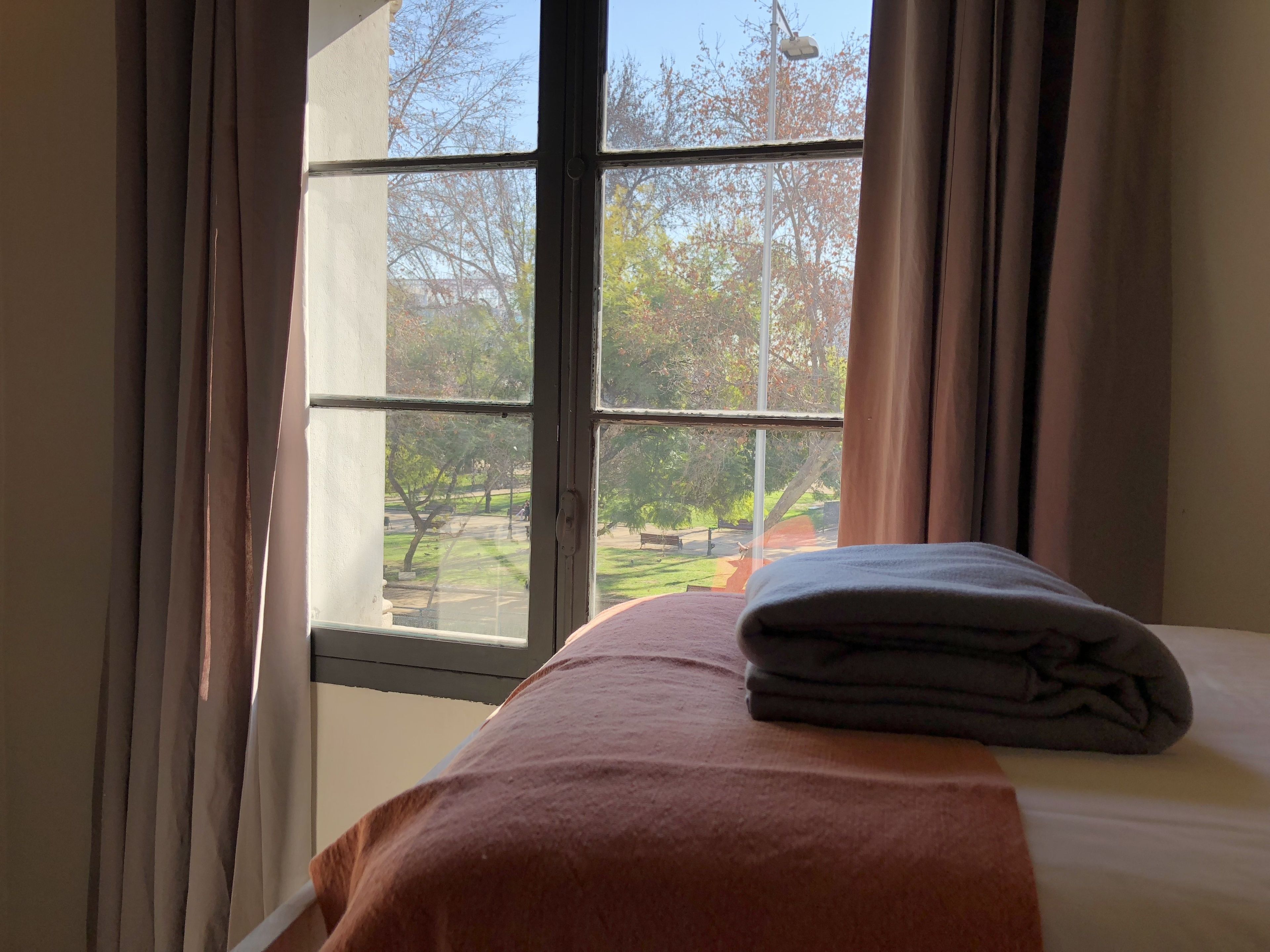 Una habitación con cama, ventana con cortinas y vistas a un parque.