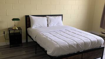 Ein Einzelbett mit Holzrahmen und weißer Bettwäsche in einem Zimmer mit Backsteinwand und Holzboden.