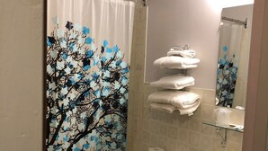 A bathroom with a shower curtain featuring a tree design, a toilet, a sink with a marble countertop, and a stack of towels. - Spanish River Inn (Spanish)