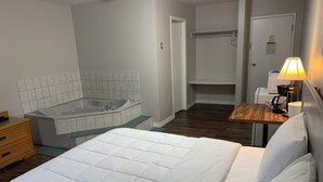 A hotel room with a bed, a wooden nightstand, a lamp, a bathroom with a bathtub, and a shower area. - Spanish River Inn (Spanish)