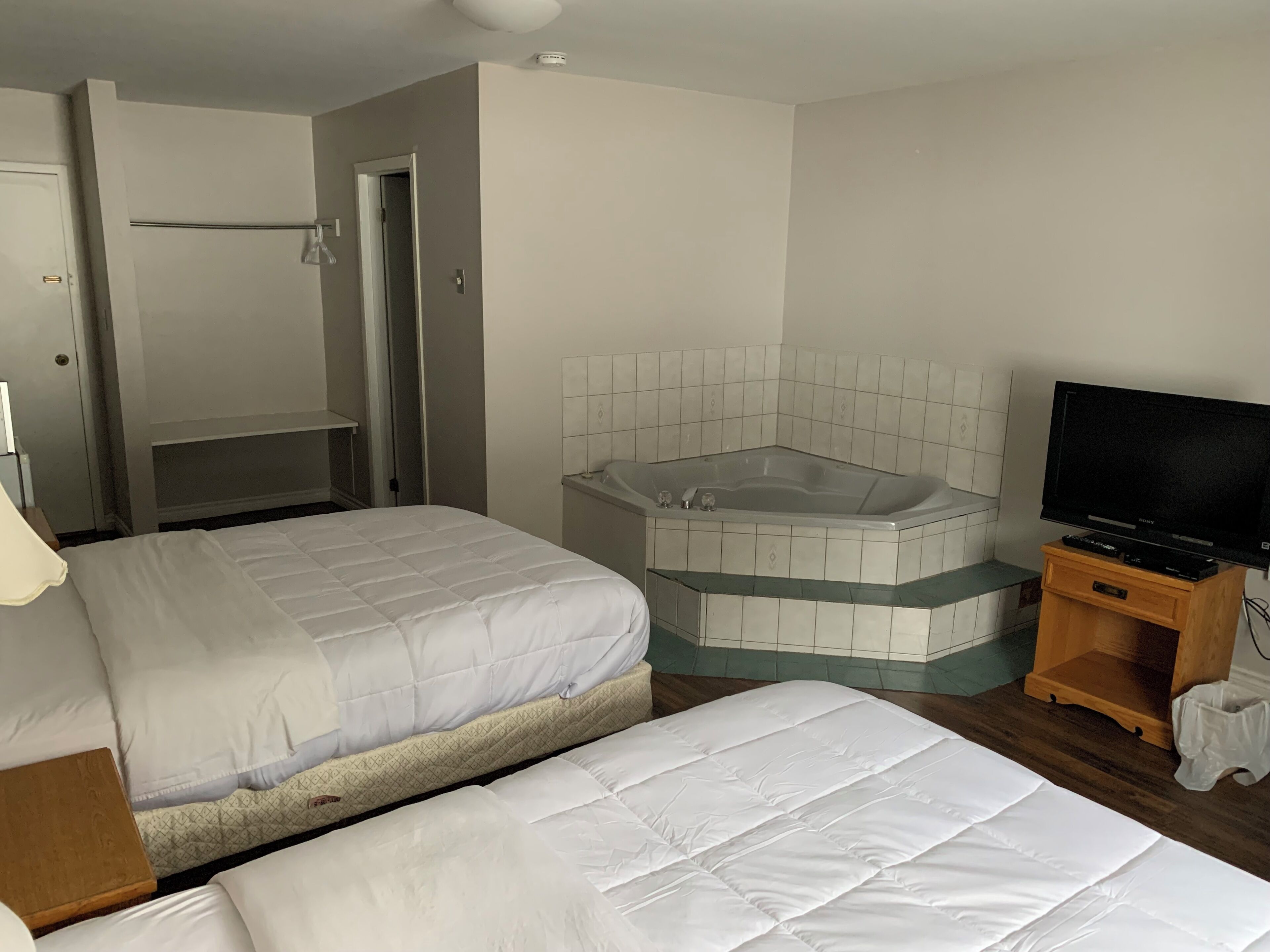 A hotel room with two beds, a bathtub, a television, and a wooden cabinet.