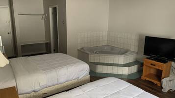 A hotel room with two beds, a bathtub, a television, and a wooden cabinet.