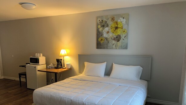 A hotel room with a bed, a desk with a microwave, a coffee maker, and a lamp. - Spanish River Inn (Spanish)