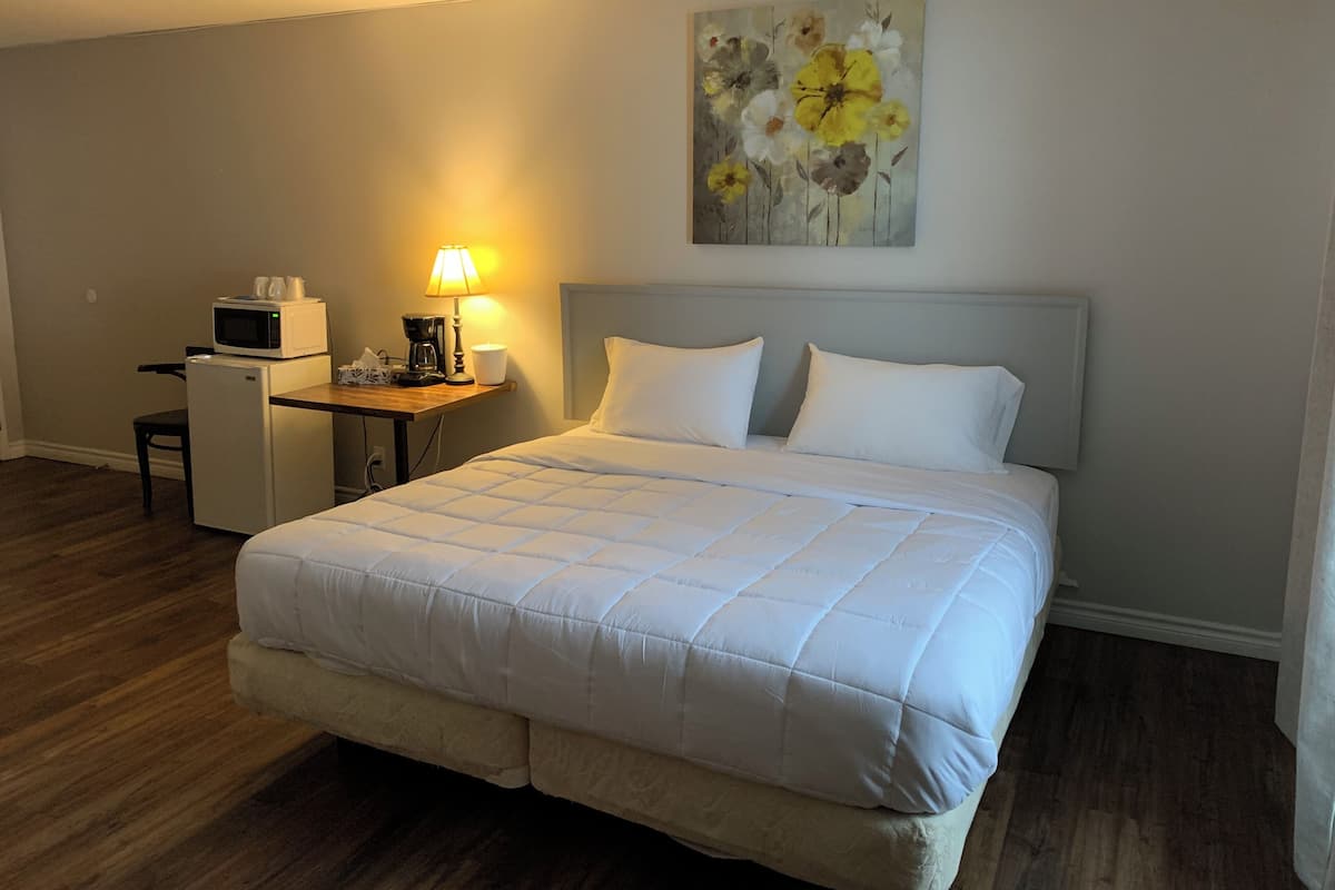 Una habitación de hotel con una cama, un escritorio con microondas, cafetera y una lámpara.