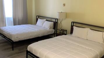 Two single beds with wooden frames and white bedding, a bedside table with a lamp, and a window with curtains.