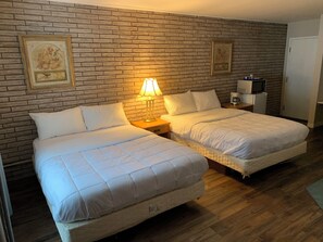 A room with two beds, a brick wall, a lamp, a coffee maker, and a television. - Spanish River Inn (Spanish)