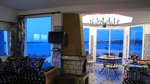 Una sala de estar con chimenea de piedra, televisor y vista al mar.