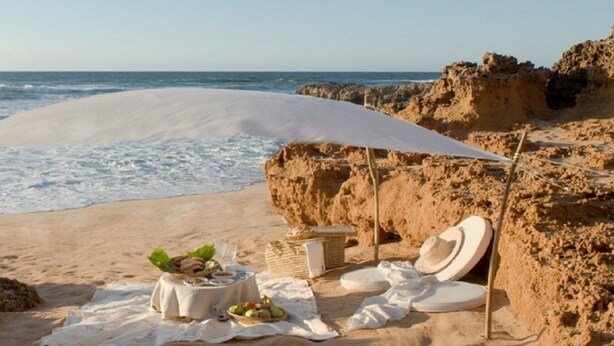 Una playa con una zona arenosa, una pequeña mesa con comida y una sombrilla.