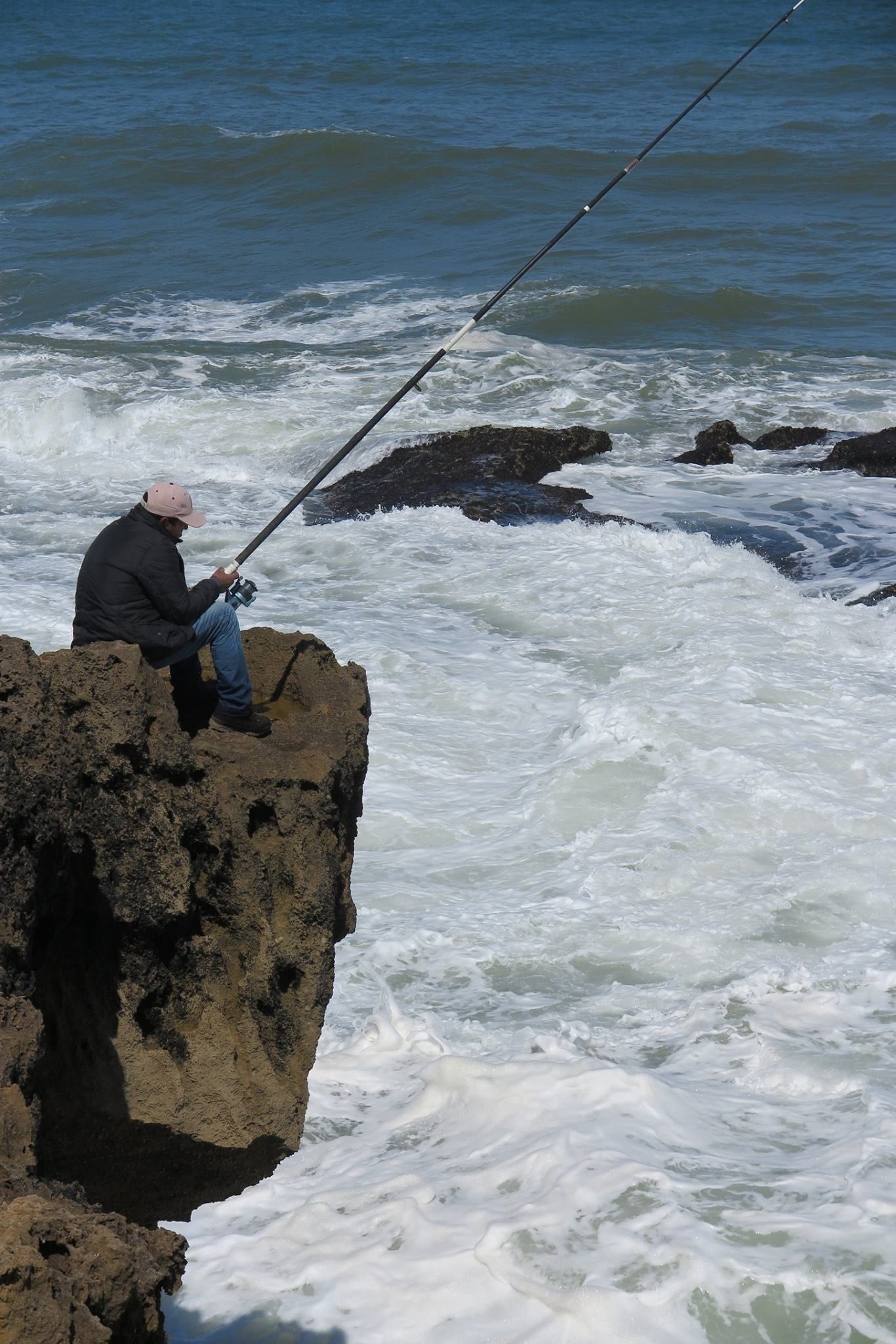 Iemand aan het vissen op een rotsachtige richel aan de zee.