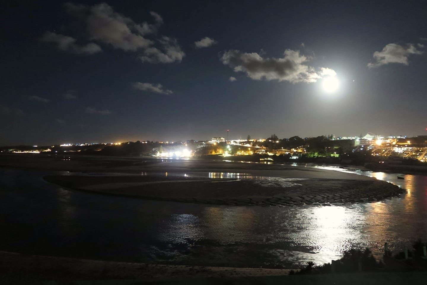 Vista nocturna de una zona ribereña con edificios iluminados al fondo.