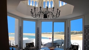 Comedor con vistas a la playa, una araña de cristal y sillas estampadas.