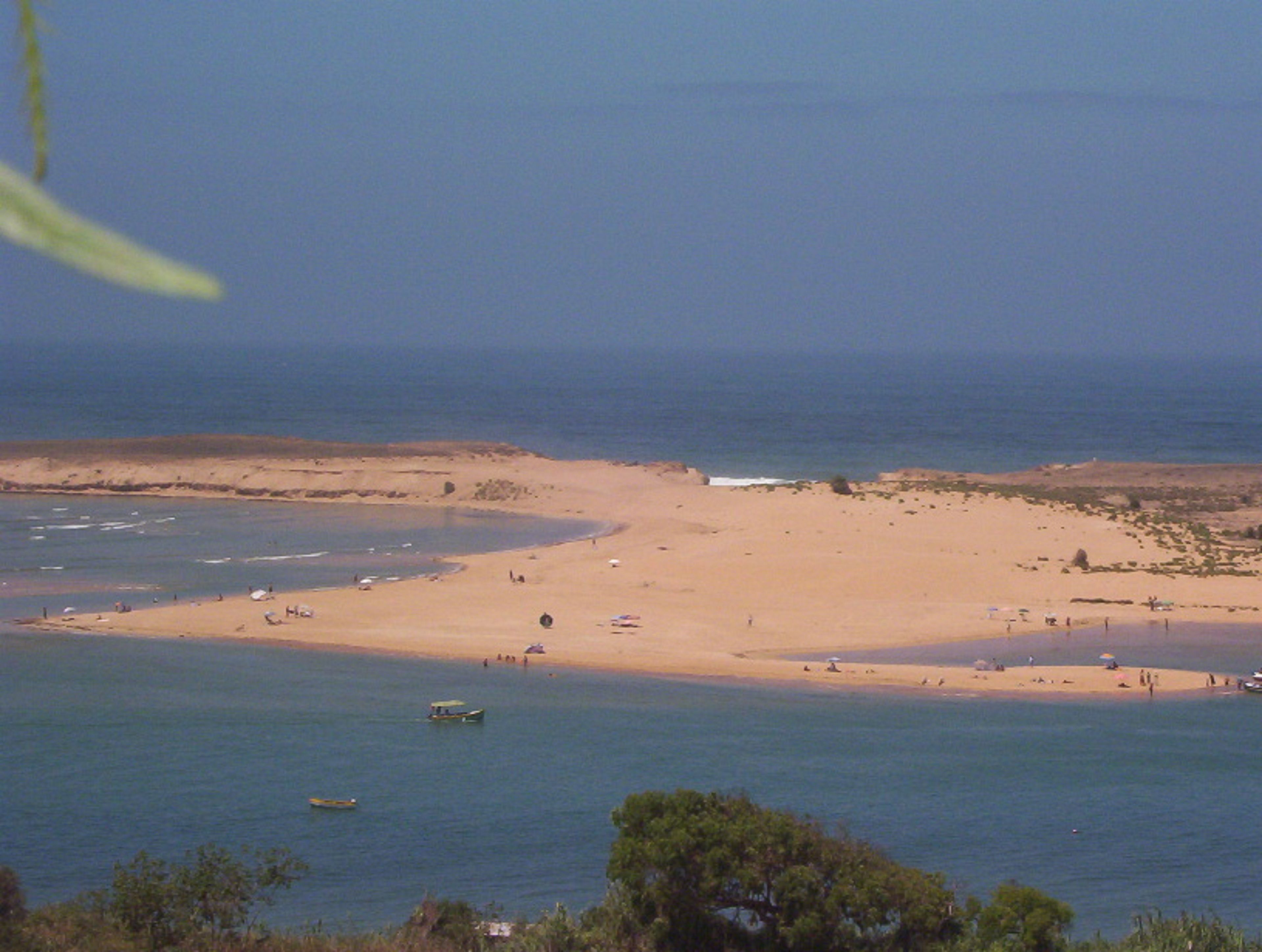 Una playa con agua azul cristalina, una orilla arenosa y algunas embarcaciones.